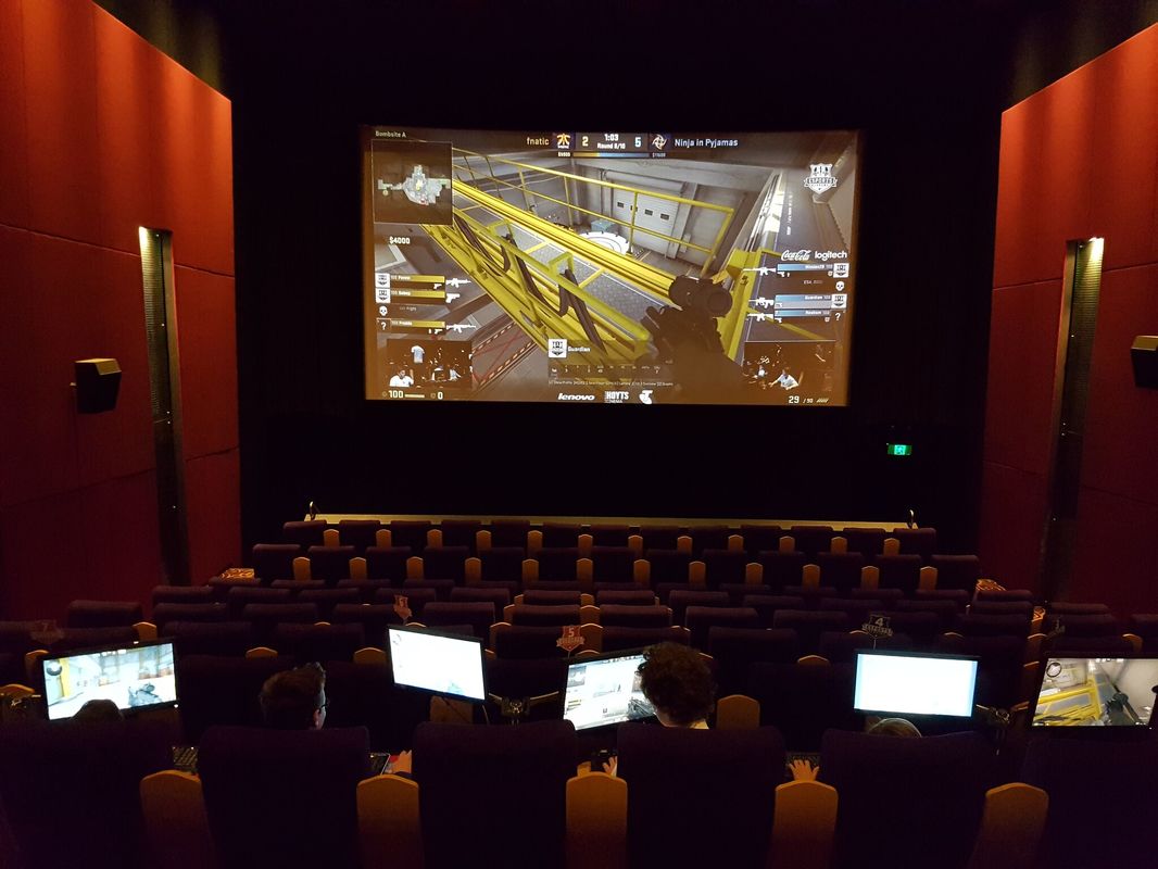Esports tournament playing on the big screen of a cinema with players seated below